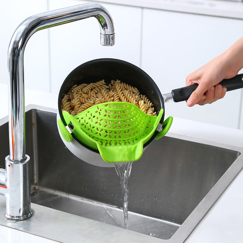 Green silicone strainer clipped to a pot of pasta, draining into a sink