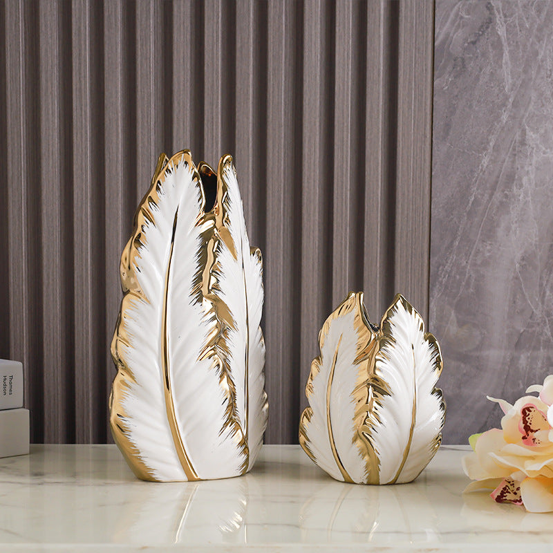 Tall and short white leaf-shaped ceramic vases with gold edges on a marble shelf
