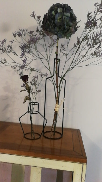 Two black wire vases holding dried flowers on a wooden cabinet