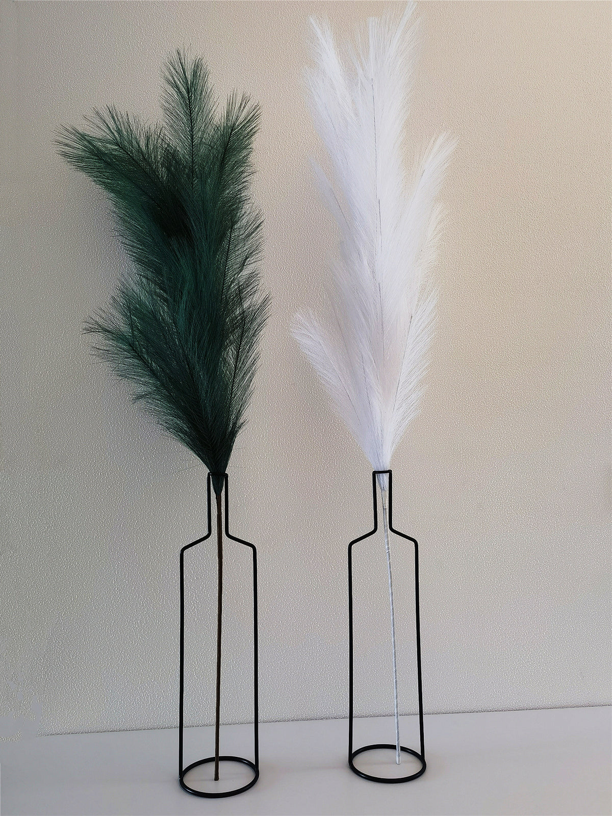 Two black wire bottle vases holding green and white faux pampas stems