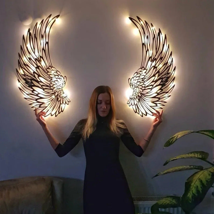 Pair of black metal angel wing wall decorations with warm lights, shown with a person for scale