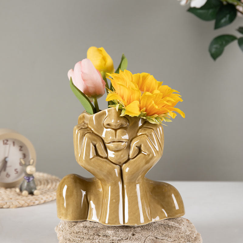 Mustard yellow ceramic face vase holding faux tulips and a sunflower