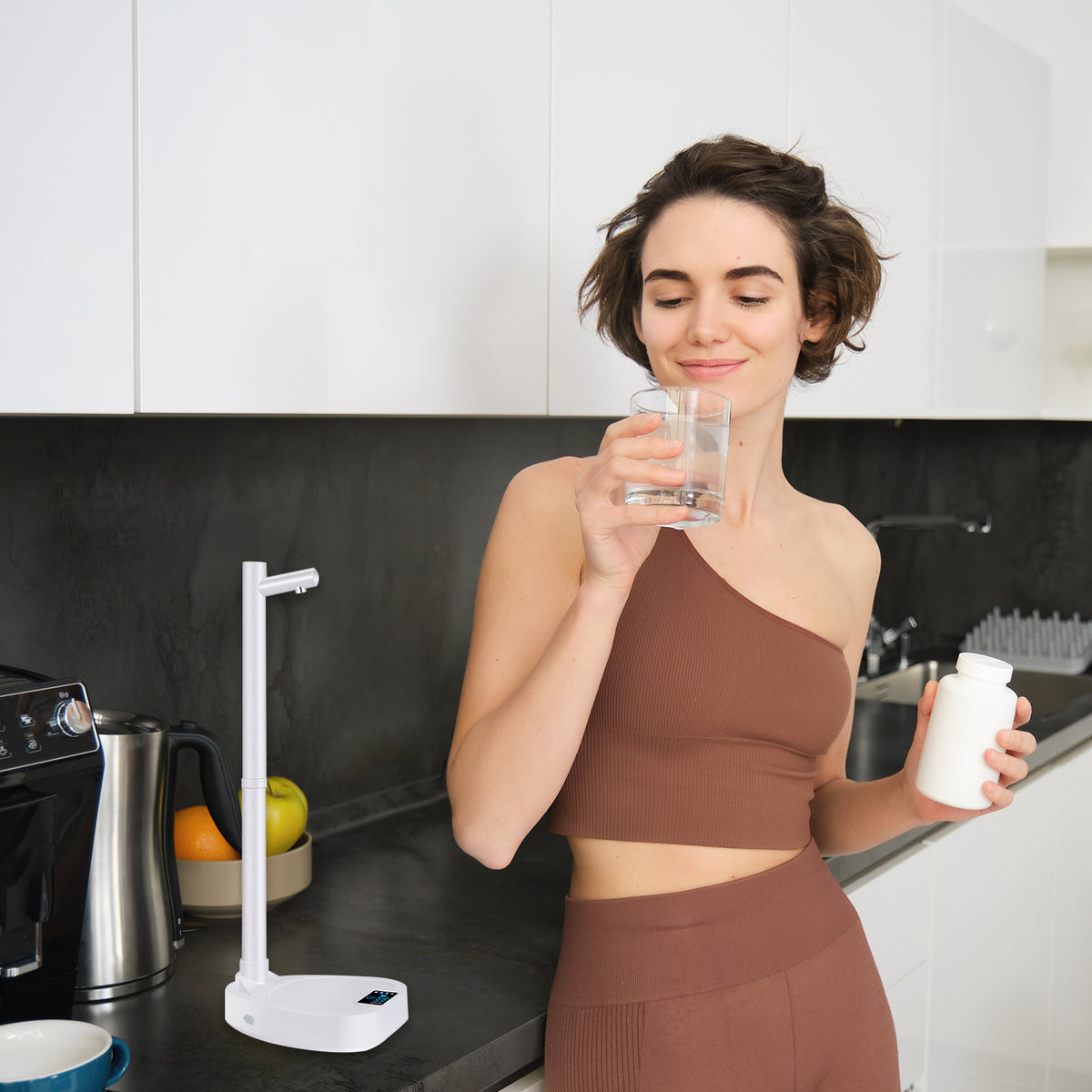 Person drinking water next to a white water dispenser pump on a kitchen counter
