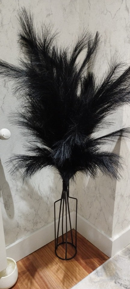 Black wire vase holding black faux pampas grass in a room corner