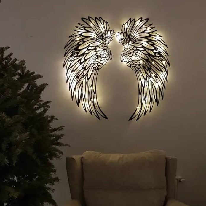 Pair of lit metal angel wings on a living room wall above an armchair