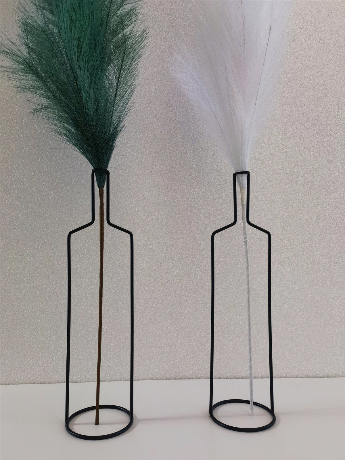 Close view of two black wire bottle vases with faux pampas stems