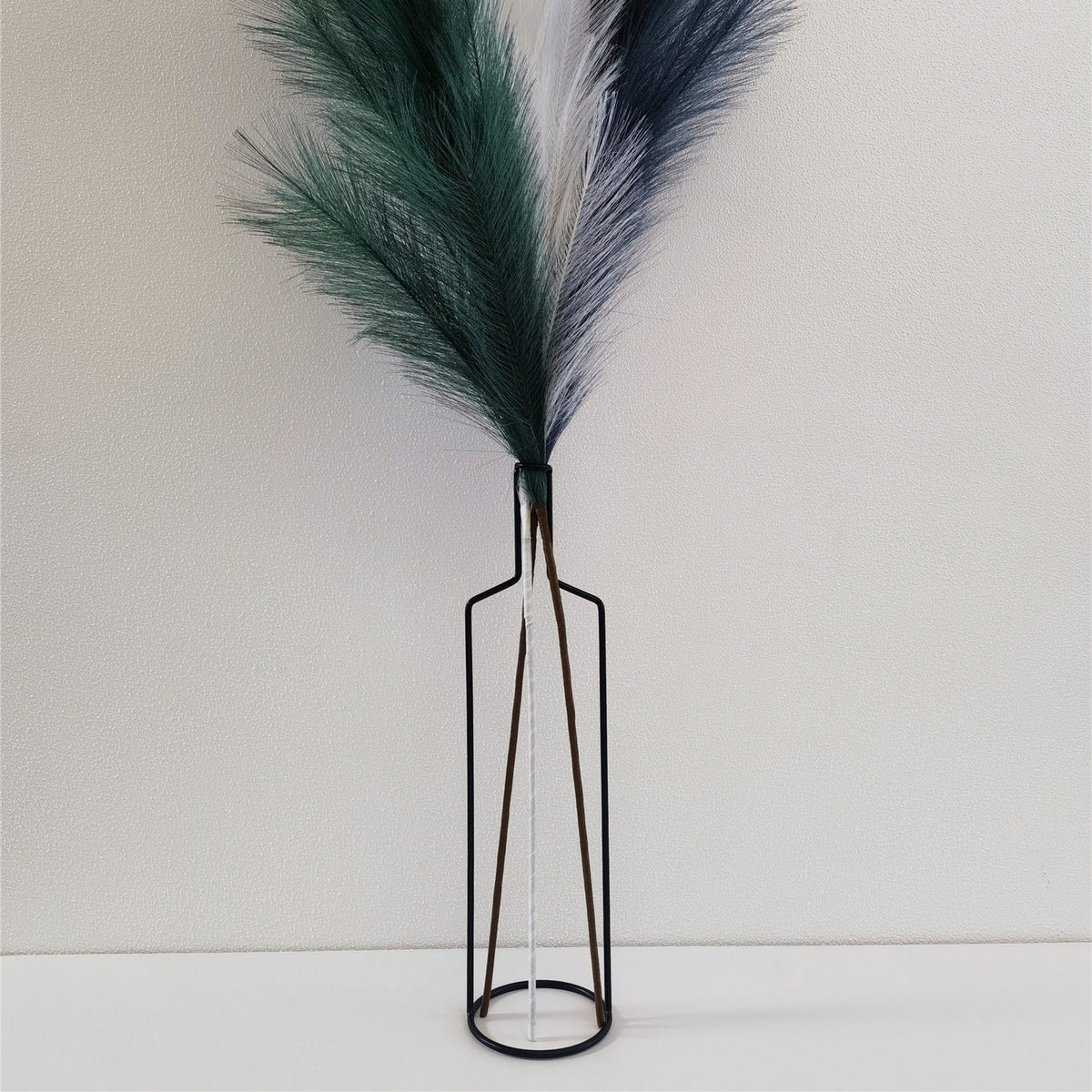 Black wire bottle-shaped vase holding green and white faux pampas stems