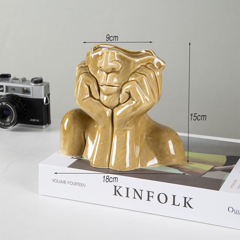 Mustard yellow ceramic face vase, 15 cm high and 18 cm wide, on a stack of books