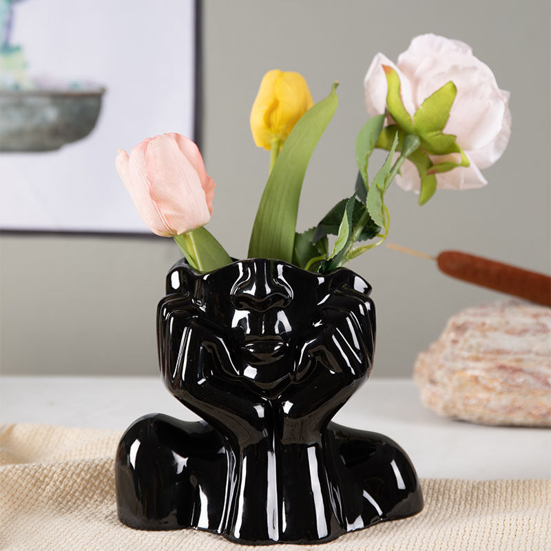Black ceramic face vase holding faux tulips and a pink rose