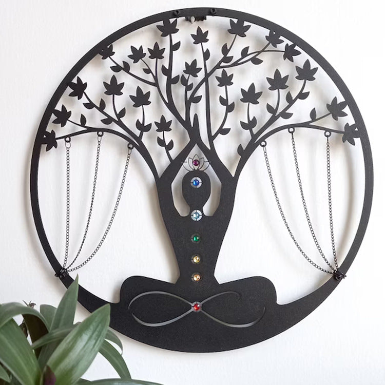 Round black metal wall art of a meditating figure forming a tree of life, with hanging chains and colored gems